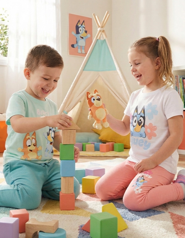 Twee kinderen spelen samen op een kleurrijk kleed, stapelen blokken en houden een speeltje vast in een lichte en vrolijke kamer.