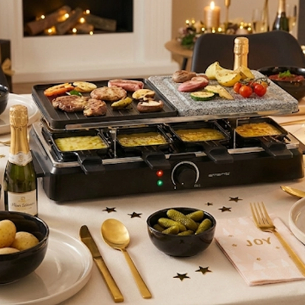 Een feestelijke eettafel met een raclettegrill met gekookt vlees en groenten, omringd door schalen met bijgerechten, champagne en kaarsen.