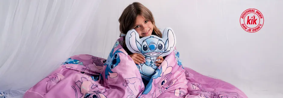 Een kind is gewikkeld in een roze deken met Stitch-thema, houdt een Stitch-knuffel vast en zit tegen een zachte witte achtergrond.