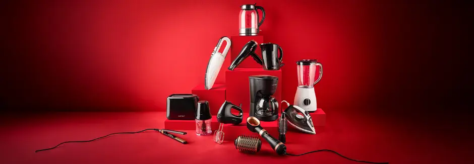Een verscheidenheid aan keuken- en schoonheidsapparaten, gerangschikt op rode blokken, waaronder een waterkoker, blender, stofzuiger en haarstylingapparaten.