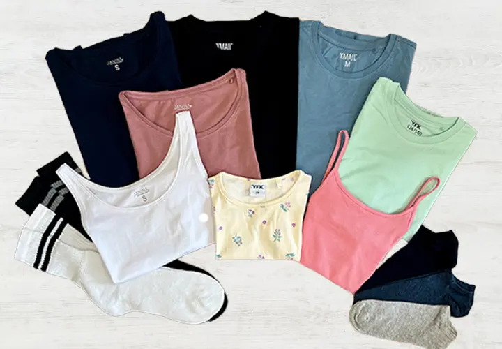 Een flatlay van diverse kleurrijke tops en sokken, waaronder tanktops en T-shirts in tinten blauw, roze, groen, wit en geel.