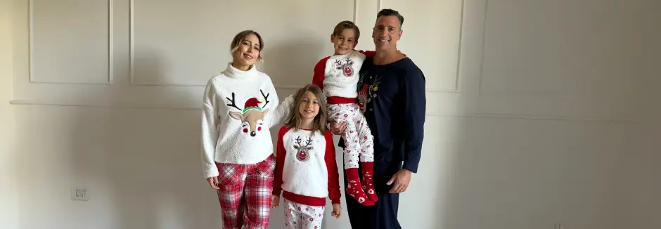 Een gezin gekleed in feestelijke kersttruien en pyjama's poseert samen en laat seizoensgebonden ontwerpen van rendieren en sneeuwvlokken zien.
