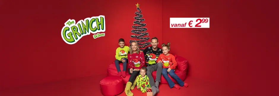 Een gezin gekleed in kleurrijke kersttruien poseert op rode zitzakken voor een feestelijke boom tegen een bijpassende rode achtergrond.