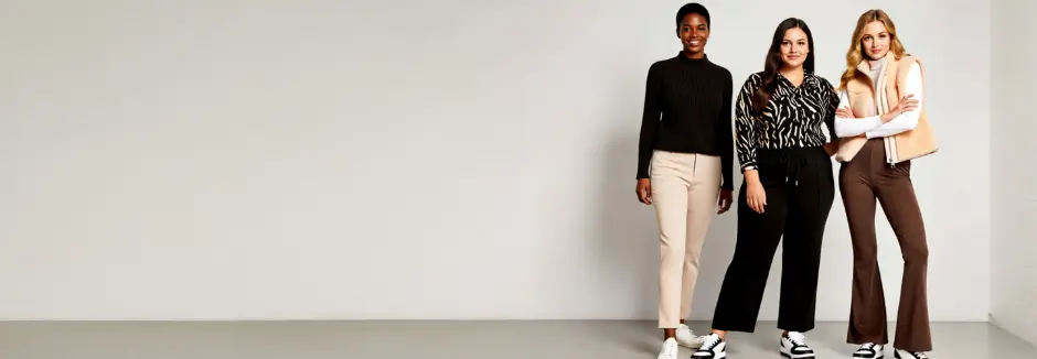 Drei Frauen in stilvollen Outfits posieren gemeinsam und präsentieren vor einem minimalistischen Hintergrund eine Mischung aus lässiger und trendiger Kleidung.