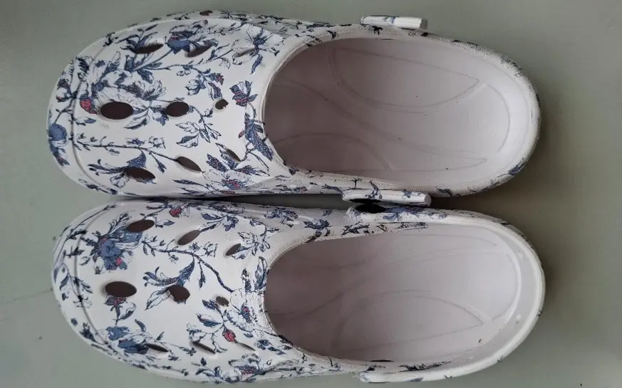 Witte klompen met bloemmotief en ventilatiegaatjes, van bovenaf gezien, rustend op een vlakke ondergrond.