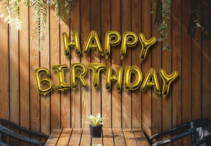Gouden ballonnen met de tekst „Happy Birthday” tegen een houten muur.