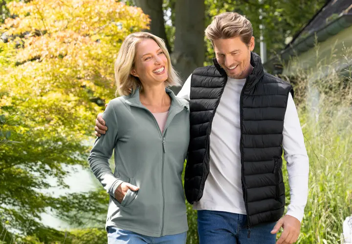 Een stel geniet van een wandeling in de buitenlucht, omringd door groen en bomen, allebei casual en comfortabel gekleed.