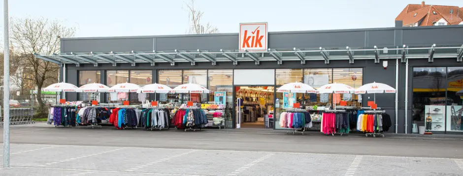 Buitenaanzicht van een KiK-winkel met KiK-logo op de deur en kledingrekken bij de ingang