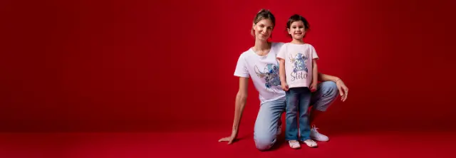 Een vrouw en een kind poseren voor een felrode achtergrond dragen bijpassende Lilo & Stitch T-shirts en casual jeans