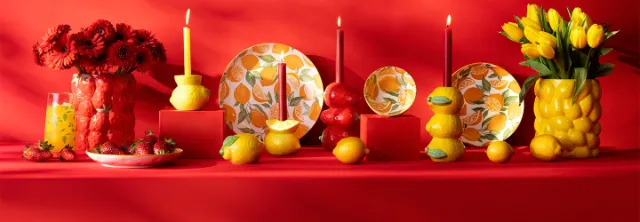 Kleurrijk gedekte tafel in rode en gele tinten met bloemstukken, decoratieve borden, citroenen en kaarsen.