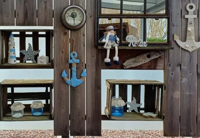 Een rustieke houten muur is voorzien van nautische decoraties, waaronder een klok, een anker, planken, zeesterren en een matrozenpop tegen een gezellige achtergrond.