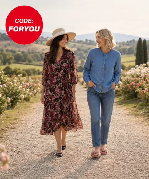 Twee vrouwen wandelen door een park in stijlvolle herfstoutfits met een trui, jurk, bodywarmer en enkellaarzen.