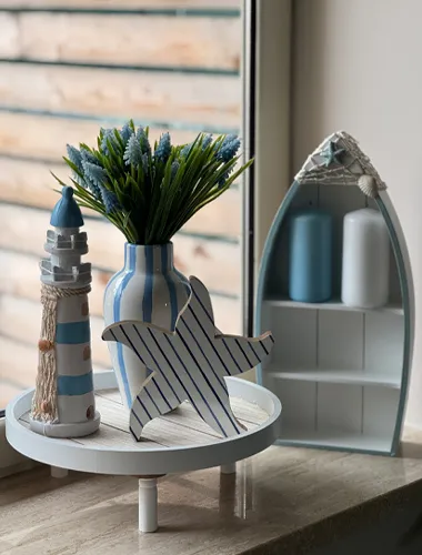 Een persoon in een spijkerjasje houdt een koffiekopje vast bij een rustieke tafel, omringd door groen en houten vaten in een buitenomgeving.