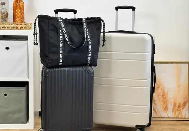 Een zwarte tas met trekkoord ligt bovenop een zwart met zilveren koffer, gerangschikt naast een witte koffer in een stijlvolle reisopstelling.