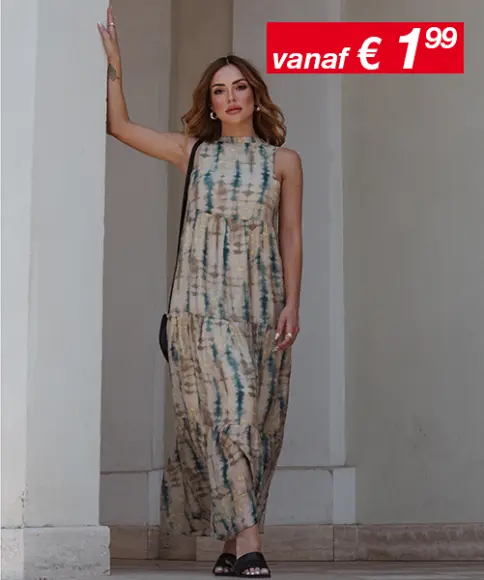 Een vrouw in een tie-dye maxi-jurk staat tegen een muur. In de hoek is een bord met prijzen te zien.