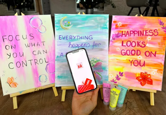 Eén hand houdt een smartphone met de KiK-app vast, daarnaast staan drie kleurrijke schilderijen met motiverende quotes op schildersezels.