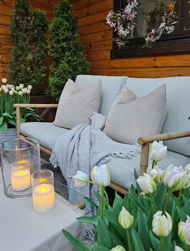 Gezellig buiten zitten met zachte kussens, een gebreid kleed, gloeiende kaarsen en bloeiende tulpen tegen een houten achtergrond.