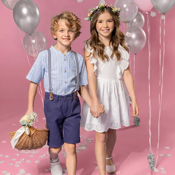 Twee kinderen houden elkaars hand vast op een roze achtergrond. De een draagt een gestreept shirt en een korte broek, de ander een witte jurk en een bloemenkroon.