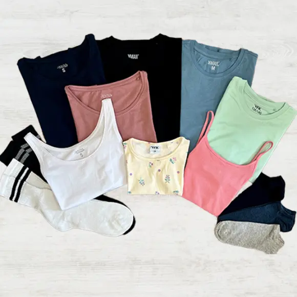 Een flatlay van diverse kleurrijke tops en sokken, waaronder tanktops en T-shirts in tinten blauw, roze, groen, wit en geel.