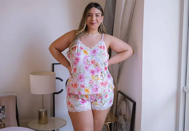 Eén persoon staat zelfverzekerd in een pyjamaset met bloemmotief, in zacht licht van een gezellige slaapkamer.