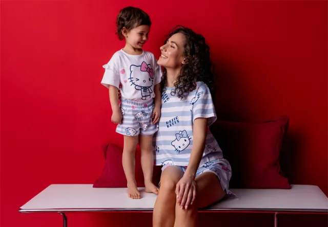 Een kind en een volwassene in een bijpassende Hello Kitty pyjama, zittend op een moderne witte tafel tegen een felrode muur.