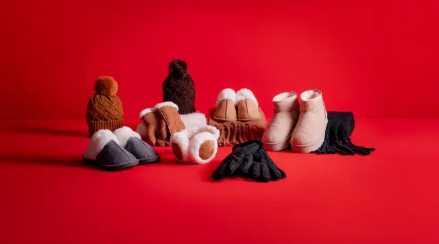 Gezellige winteraccessoires: pantoffels, handschoenen, een sjaal en mutsen tegen een felrode achtergrond