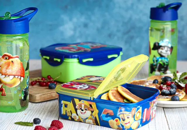 Broodtrommel en drinkflessen met PAW Patrol- en dinosaurusmotieven op een gedekte tafel met snacks en fruit voor school of de kinderopvang. Broodtrommel en drinkflessen met PAW Patrol- en dinosaurusmotieven op een gedekte tafel met snacks en fruit voor school of de kinderopvang.