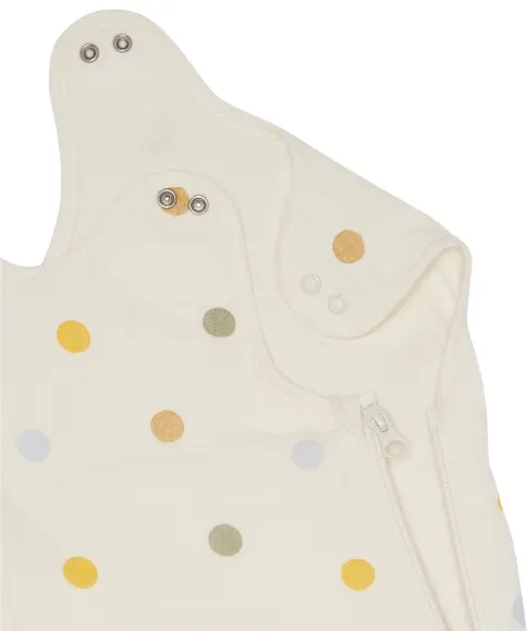 Close-up van een crèmekleurig babykledingstuk met veelkleurige stippen, drukknopen en een ritssluiting aan de zijkant.