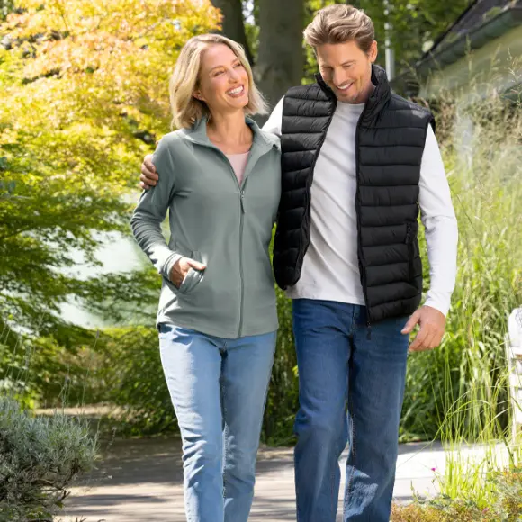 Een stel geniet van een wandeling in de buitenlucht, omringd door groen en bomen, allebei casual en comfortabel gekleed.
