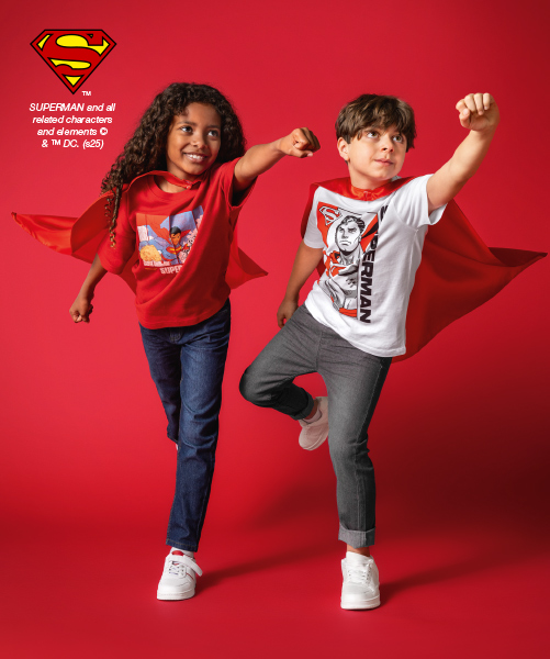 Twee kinderen in Superman pakken poseren zelfverzekerd egen een rode achtergrond en laten hun vrolijke Superman-outfits zien.