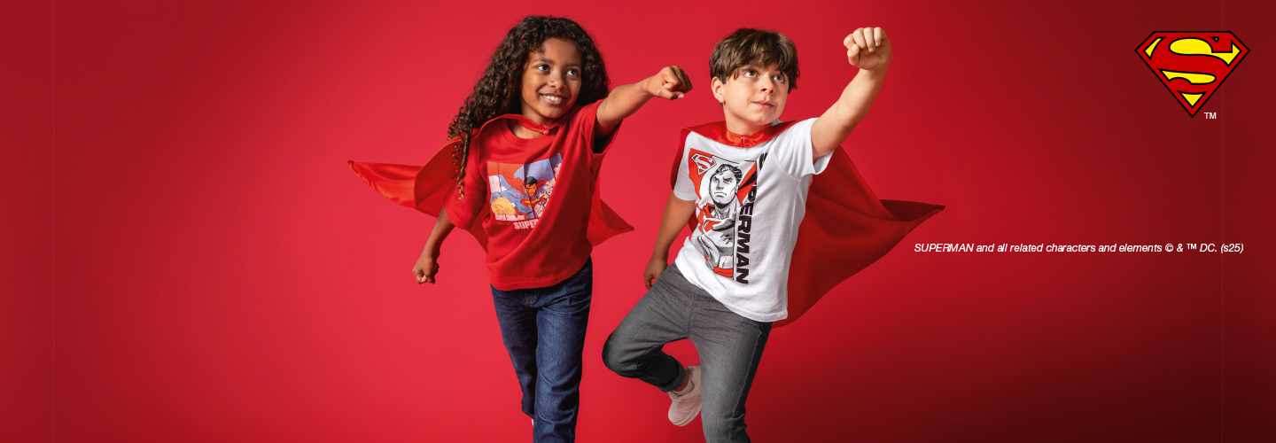 Twee kinderen in Superman pakken poseren zelfverzekerd egen een rode achtergrond en laten hun vrolijke Superman-outfits zien.