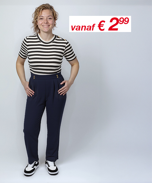 Een persoon staat zelfverzekerd in een gestreept shirt en een marineblauwe high-waisted broek, gecombineerd met zwart-witte schoenen, tegen een egale achtergrond.