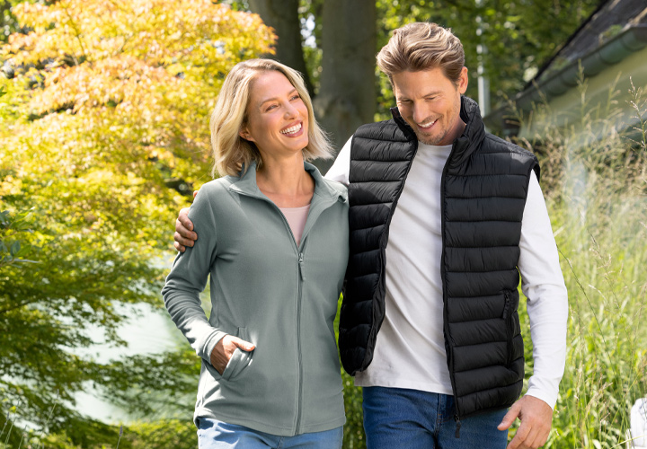 Een stel geniet van een wandeling in de buitenlucht, omringd door groen en bomen, allebei casual en comfortabel gekleed.