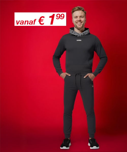 Een model staat in een strakke zwarte hoodie en bijpassende joggingbroek tegen een levendige rode achtergrond, met de handen in de zakken en sportieve sneakers aan.