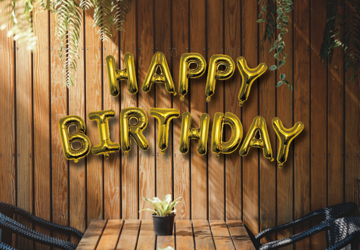 Gouden ballonnen met de tekst „Happy Birthday” tegen een houten muur.