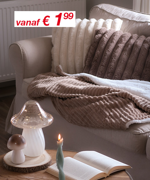 Gezellige huiskamer met zachte kussens, zachte dekens, een brandende kaars en een paddestoellamp op een houten tafel.