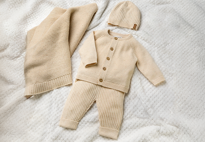 Een zacht beige babysetje met een vest, broek en bijpassend mutsje, uitgestald op een gestructureerde deken.